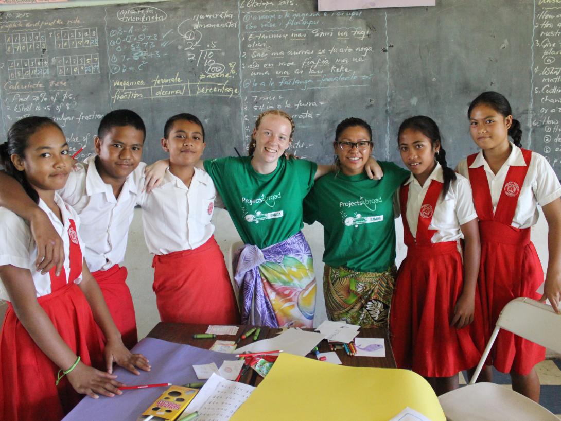 During a volunteer project in Samoa, a student teacher takes a photo with her class. On a summer volunteer program abroad, a volunteer teacher takes a photo with her Samoan students.